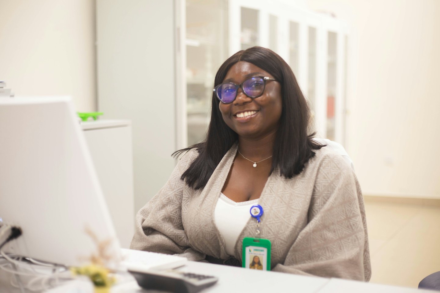 Una giovane donna sorridente con gli occhiali alla sua scrivania in ufficio.